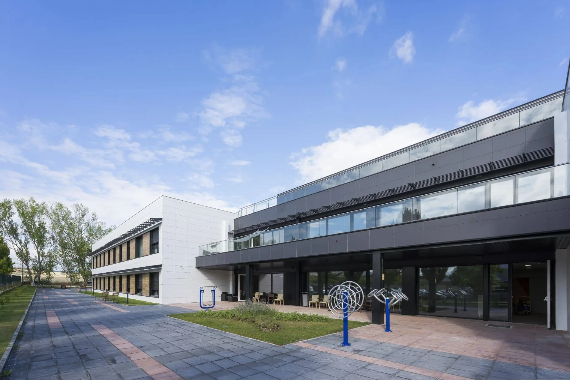Edificio educativo Passivhaus de una planta, con fachada acristalada continua y patio pavimentado