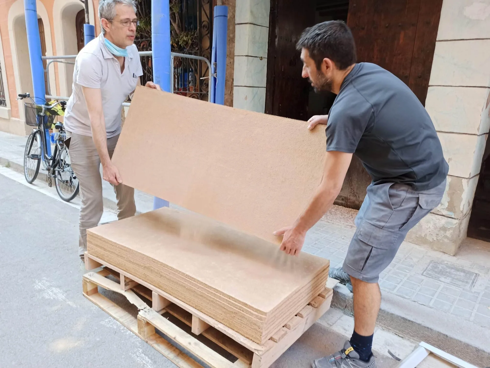 Dos operarios trasladan un panel de aislamiento a pie de obra