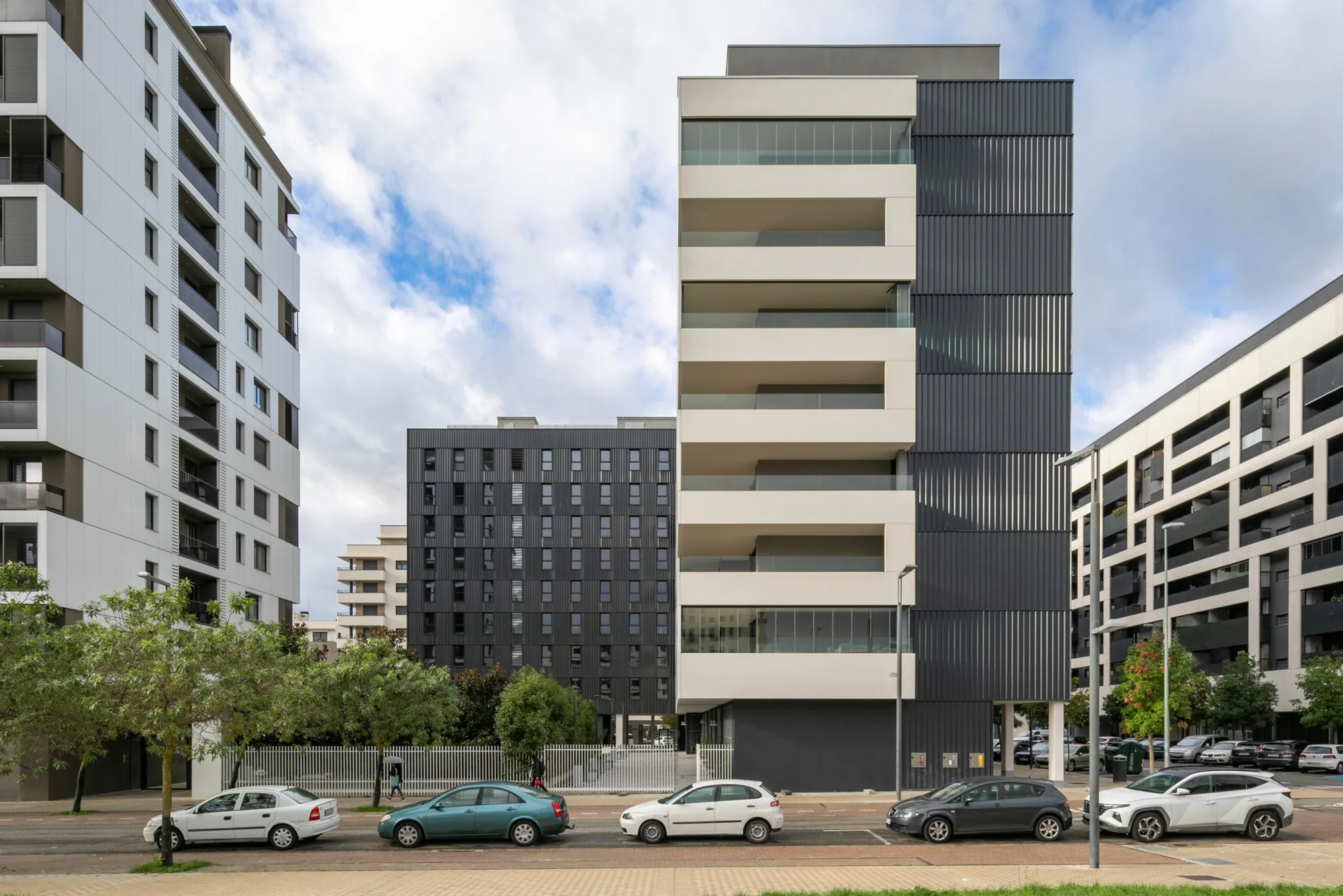 Calle con varios bloques de vivienda; en primer término, un edificio Passivhaus de fachada clara y galerías corridas