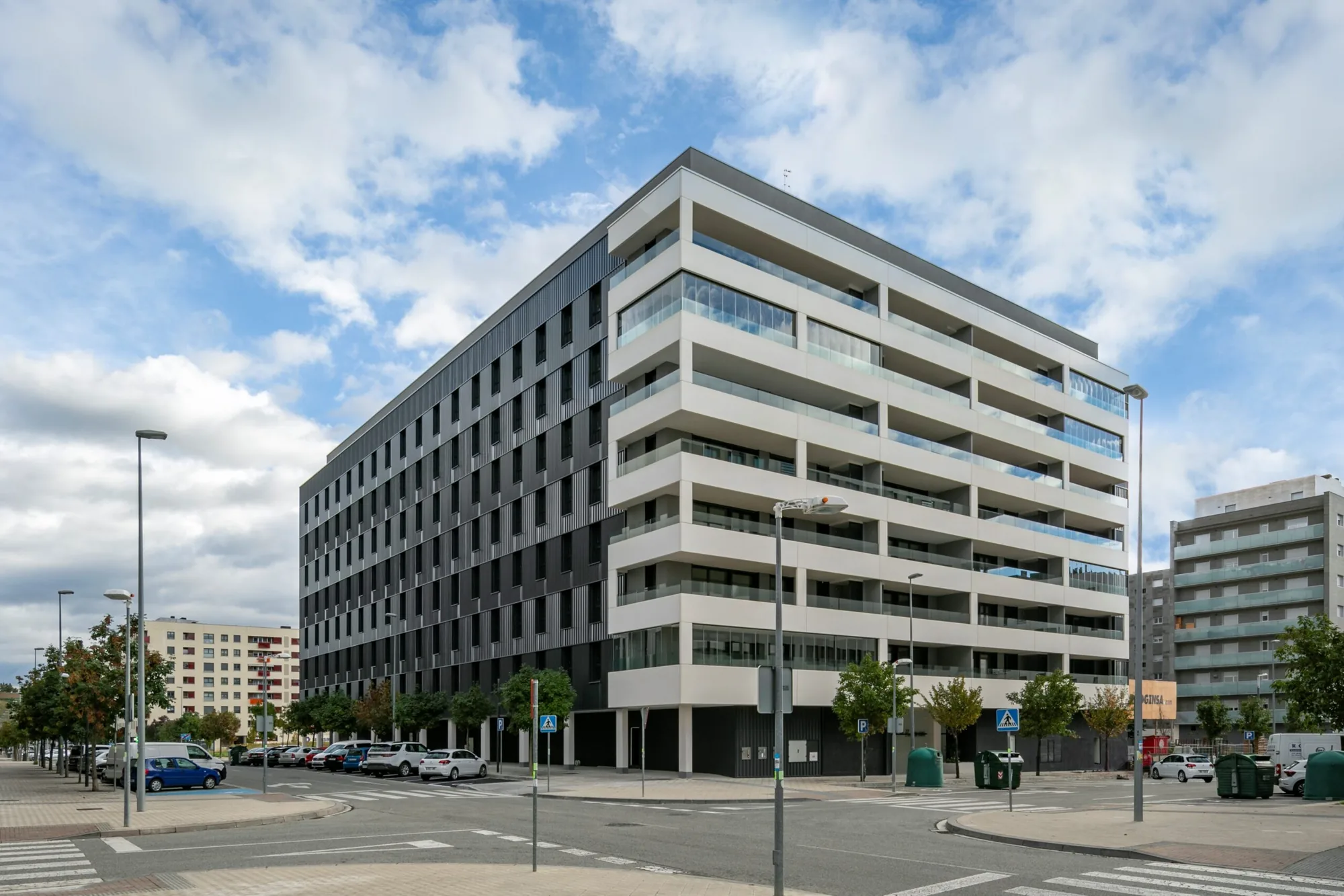 Edificio plurifamiliar Passivhaus de siete plantas visto desde la esquina, con fachada ventilada oscura y galerías acristaladas