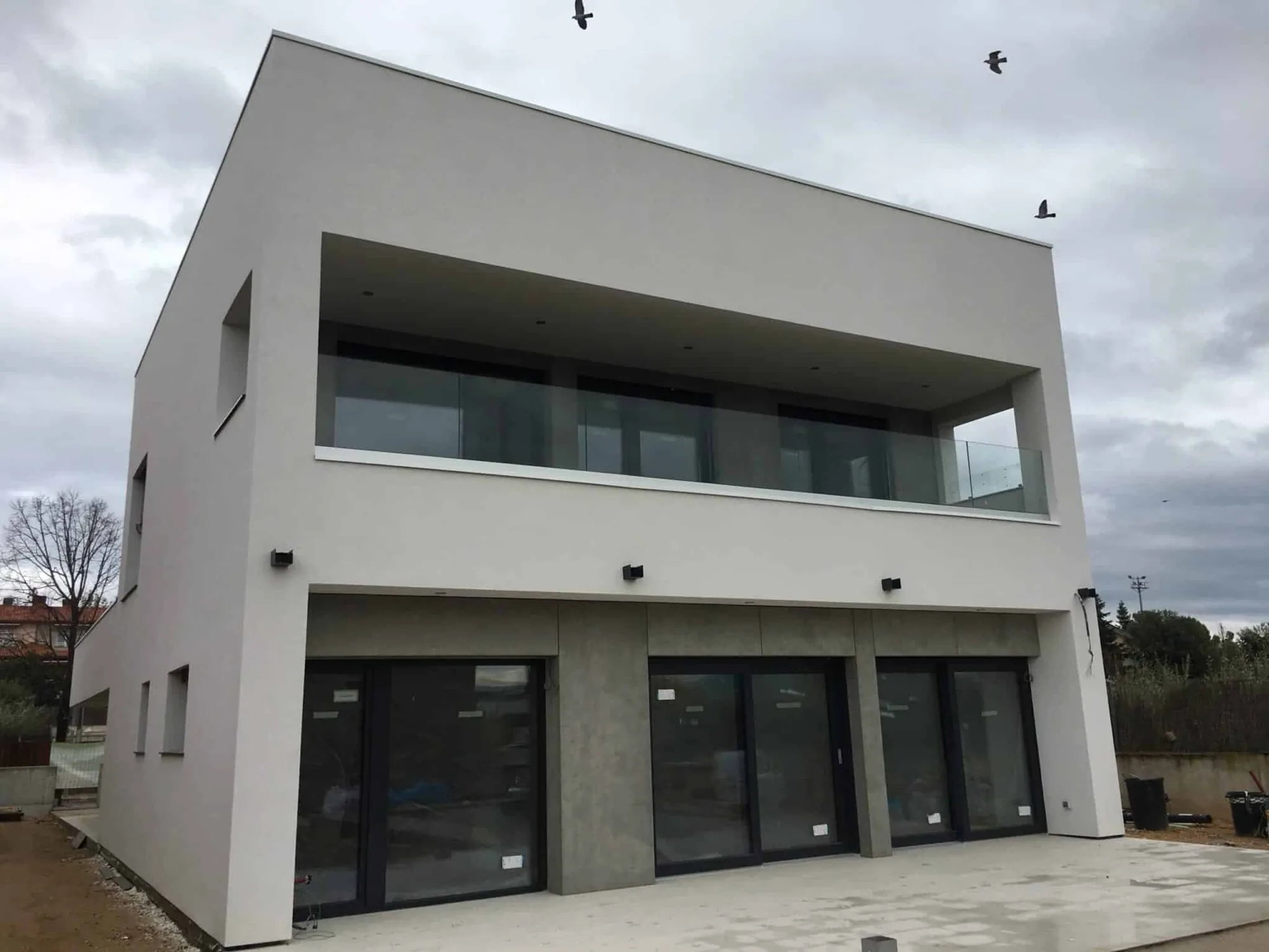 Vivienda unifamiliar de dos plantas recién terminada, con grandes huecos de carpintería oscura y el terreno aún sin urbanizar