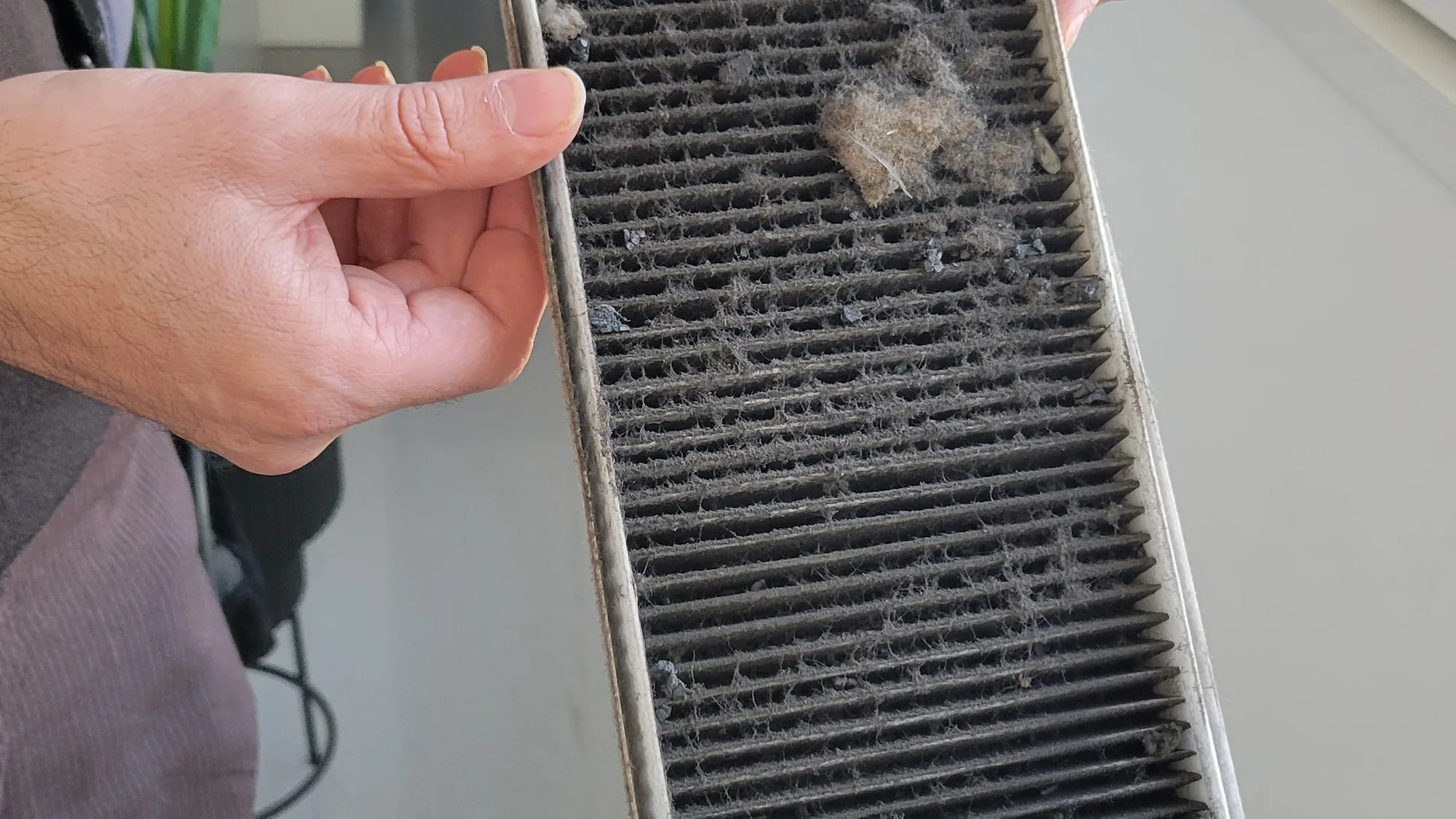 Mano sosteniendo el filtro de una ventilación de doble flujo con el polvo retenido tras meses de uso